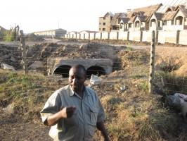 Housing built just beyond the NNP fence; Southern Bypass to be built along the dirt strip that still separates them. In the foreground is Michael Wanjau, then-Senior Warden for NNP. Photo: Glen Hyman