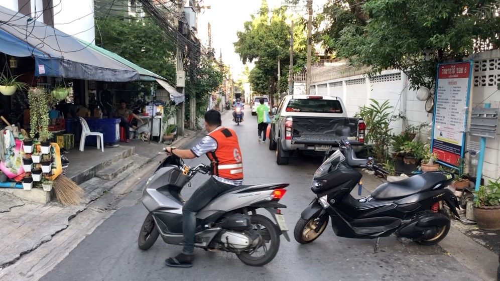 A man on a motorbike with a orange vest on a side street
