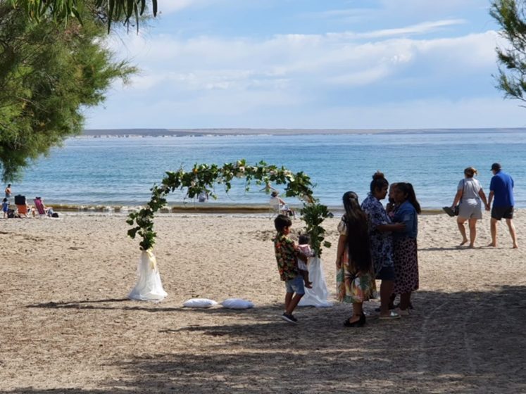 A group of people on a beach in front of a wedding arch