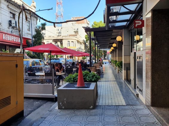 A sidewalk with outdoor restaurant seating and people