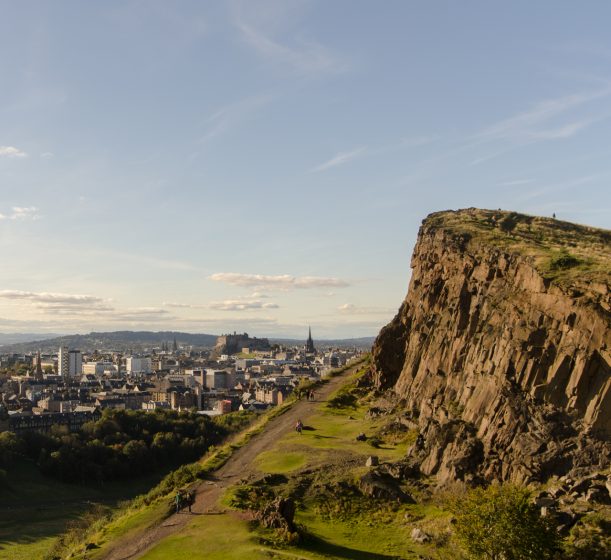 A cliff face and path overlooking a city in the distance