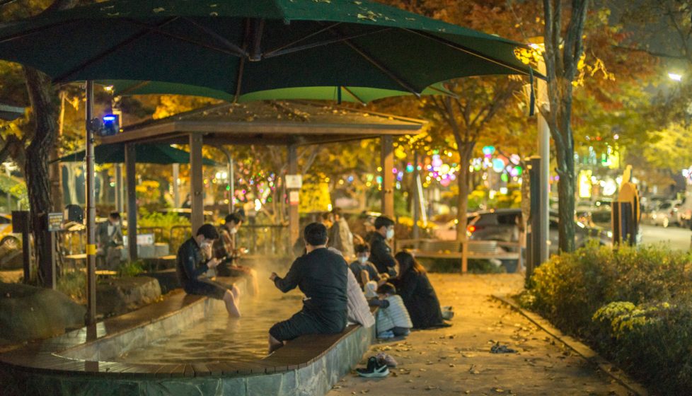 People sitting with their feet in a hot spring inside a park at night