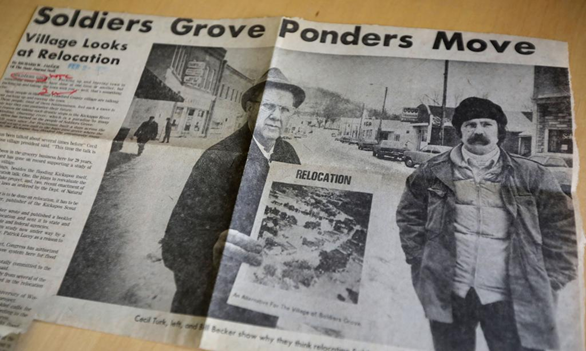 A picture of a newspaper clipping of a man holding a poster titled "Relocation" standing next to another man in the middle of a street