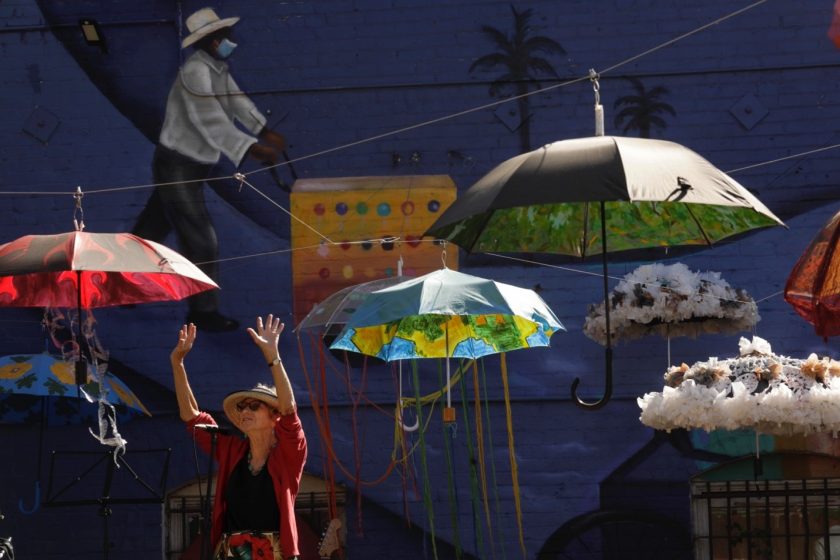 A picture of painted umbrellas hanging from string outside and a woman reaching up below them