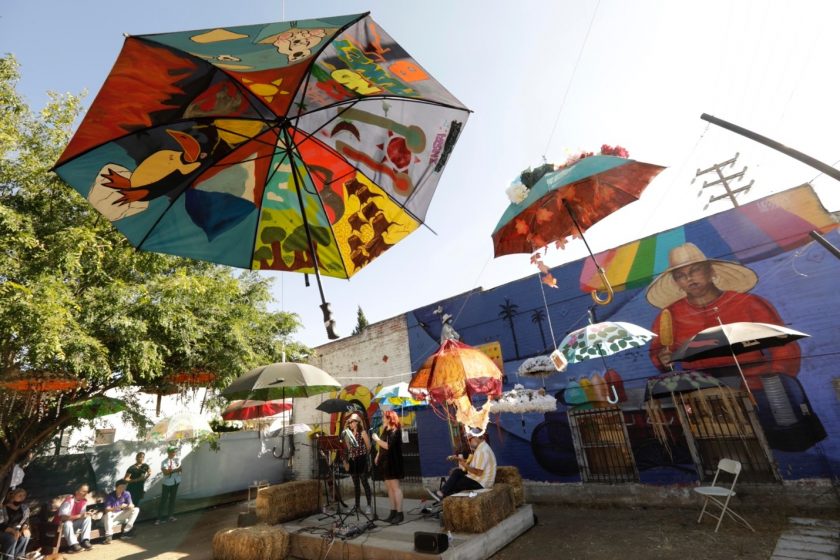 A picture of painted umbrellas hanging above a courtyard with a mural in the background and people below