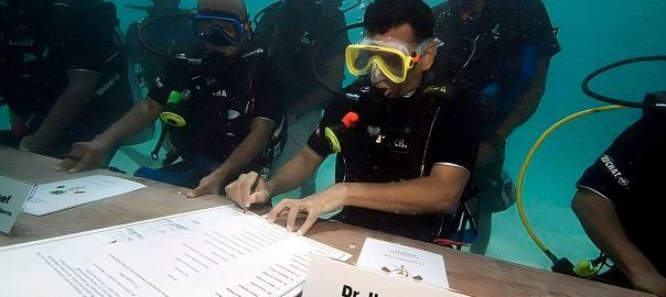 A picture of scuba divers sitting around a table with papers while underwater