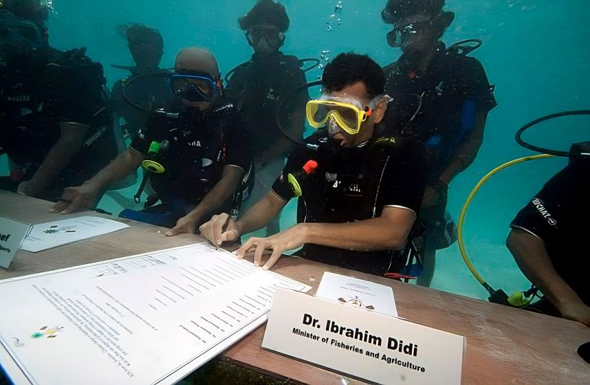 A picture of scuba divers sitting around a table with papers while underwater