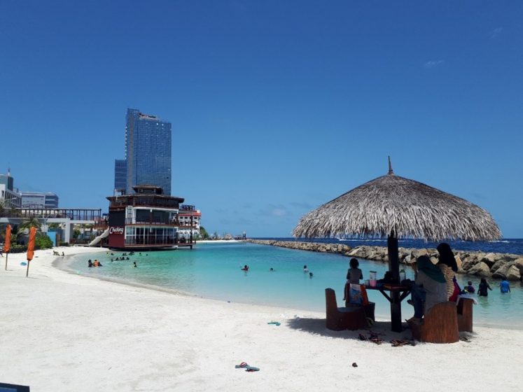 A picture of a beach with people sitting at a shaded table with a building in the distance