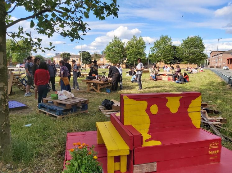 A picture of a group of people standing around in a field with wooden structures scattered about