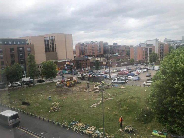 A picture of a field with a parking lot and buildings behind it