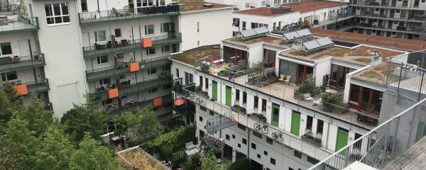 A picture of apartment buildings with green plants on balconies and in a courtyard in front of the buildings