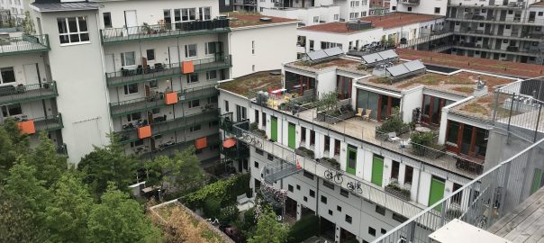 A picture of apartment buildings with green plants on balconies and in a courtyard in front of the buildings