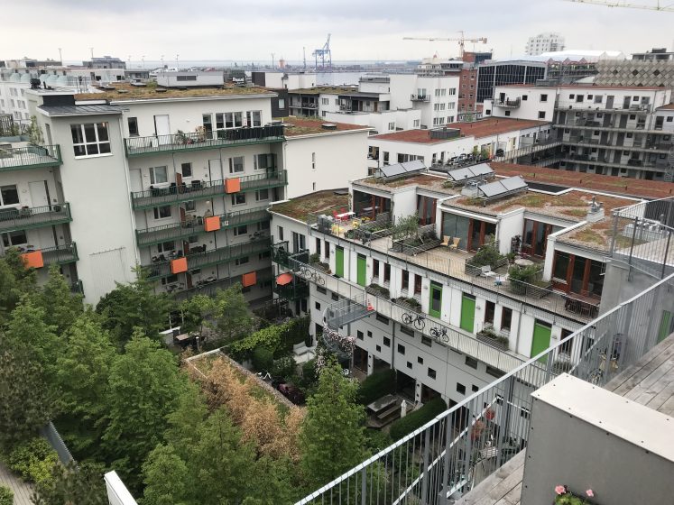 A picture of apartment buildings with green plants on balconies and in a courtyard in front of the buildings