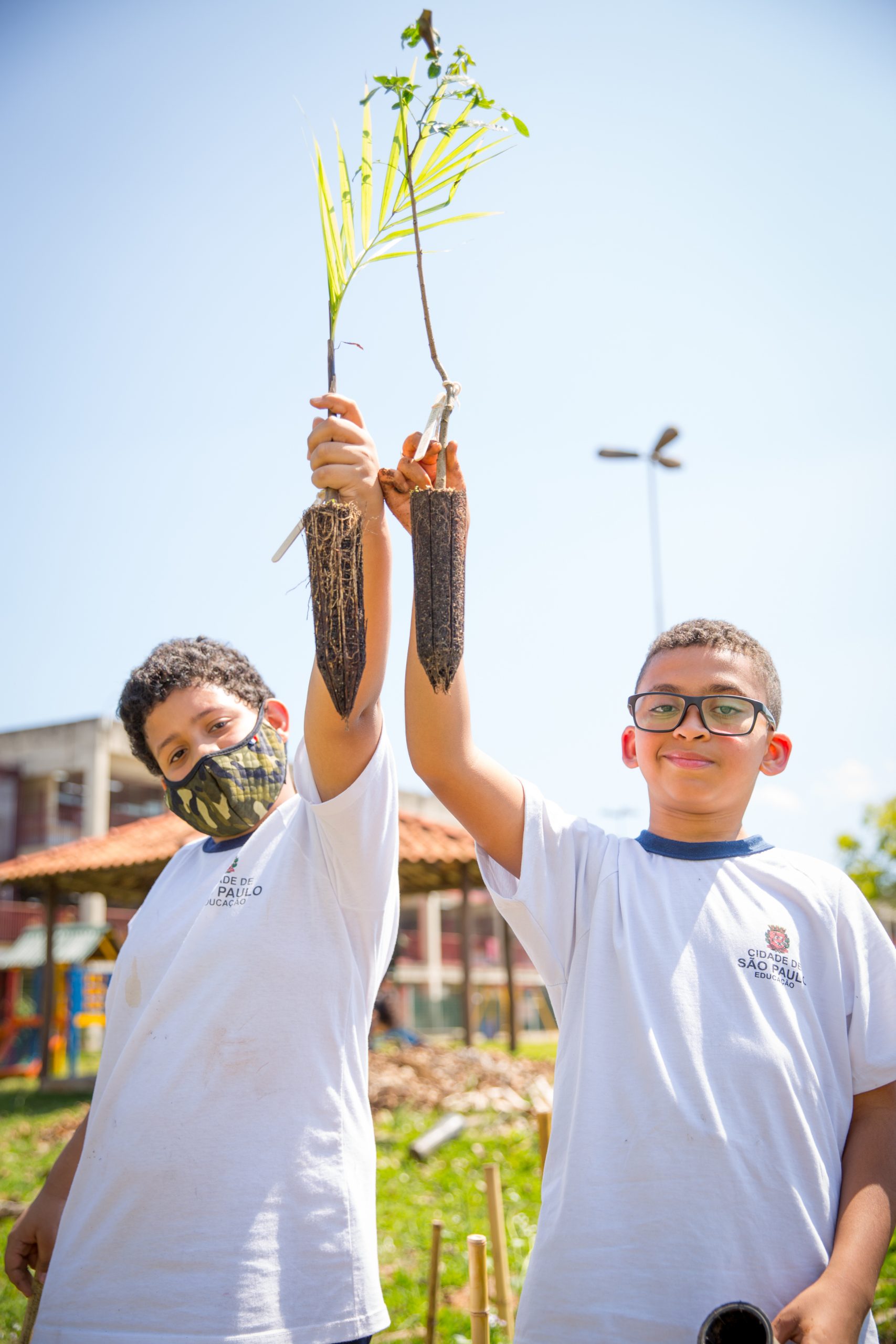 A photo for two children in white t-shirts holding up plants with roots