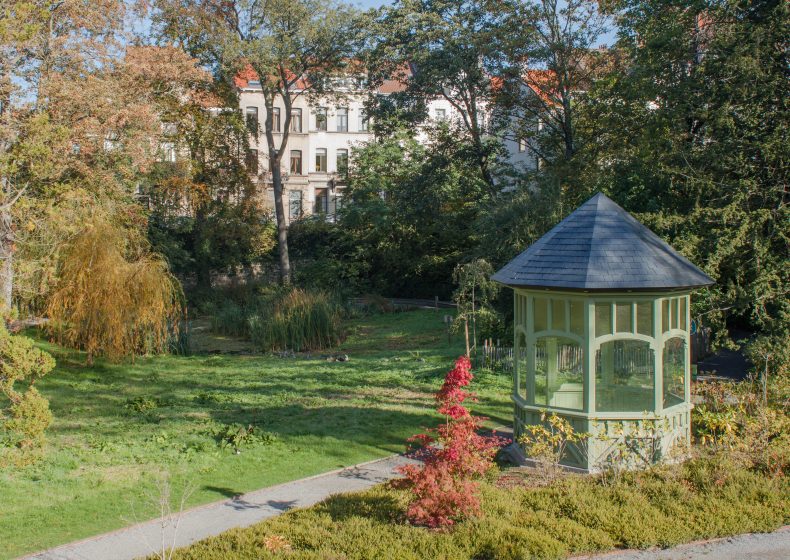 A picture of a park with trees, a gazebo, and a walking path with a building in the background