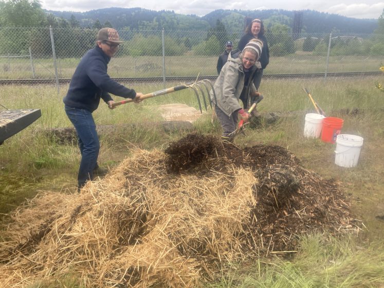 A picture of three people raking, shoveling, and tossing hay and dirt