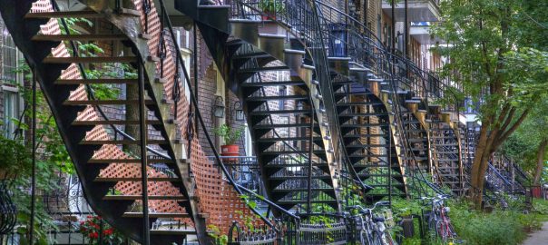 A picture of the side of a building with several metal staircases and fire escapes coming down with greenery around them