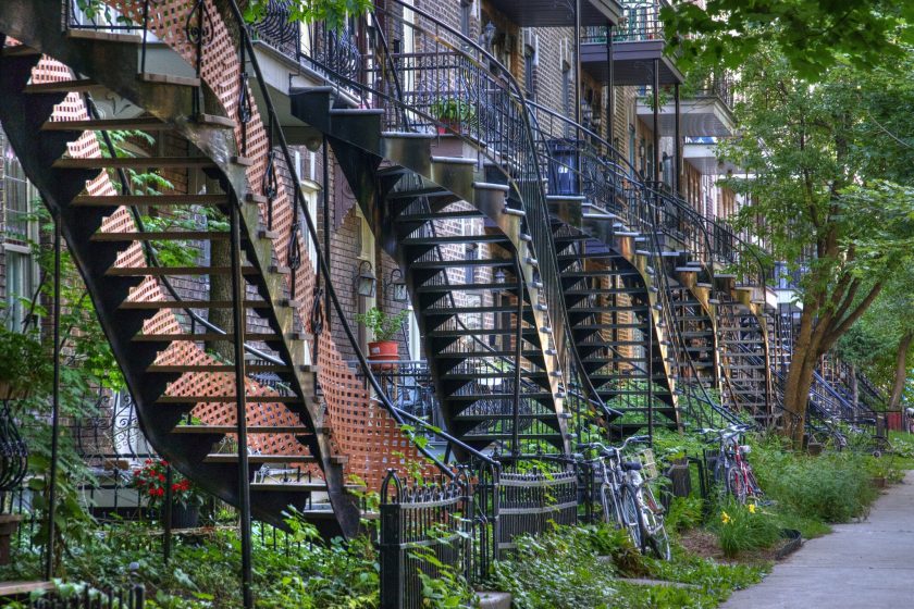 A picture of the side of a building with several metal staircases and fire escapes coming down with greenery around them