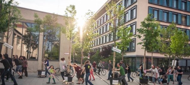 A picture of a sidewalk with people walking, cycling, and moving potted trees