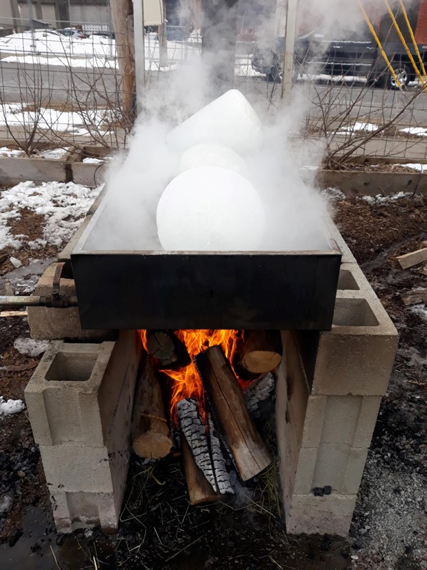 A picture of a smoking white blocks of snow inside a metal tray atop cinder blocks with a fire underneath
