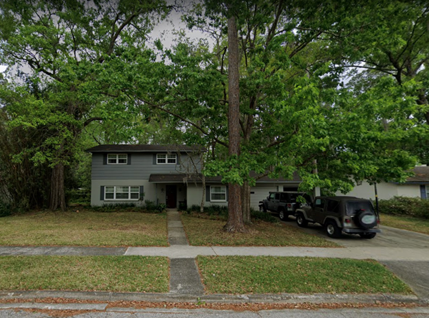 A picture of a two-story house with a large tree in the front yard and a stone path leading up to the front door