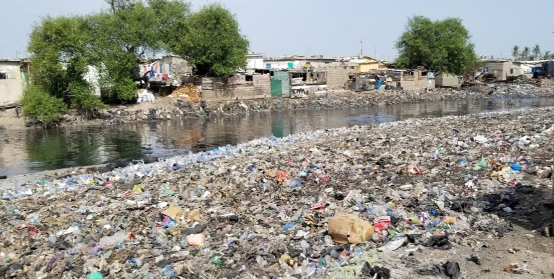 A picture of a waterway with mounds of plastic garbage on both sides of it
