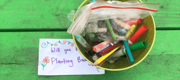 A close-up picture of a small metal bucket full of colorful writing utensils on a bright green table