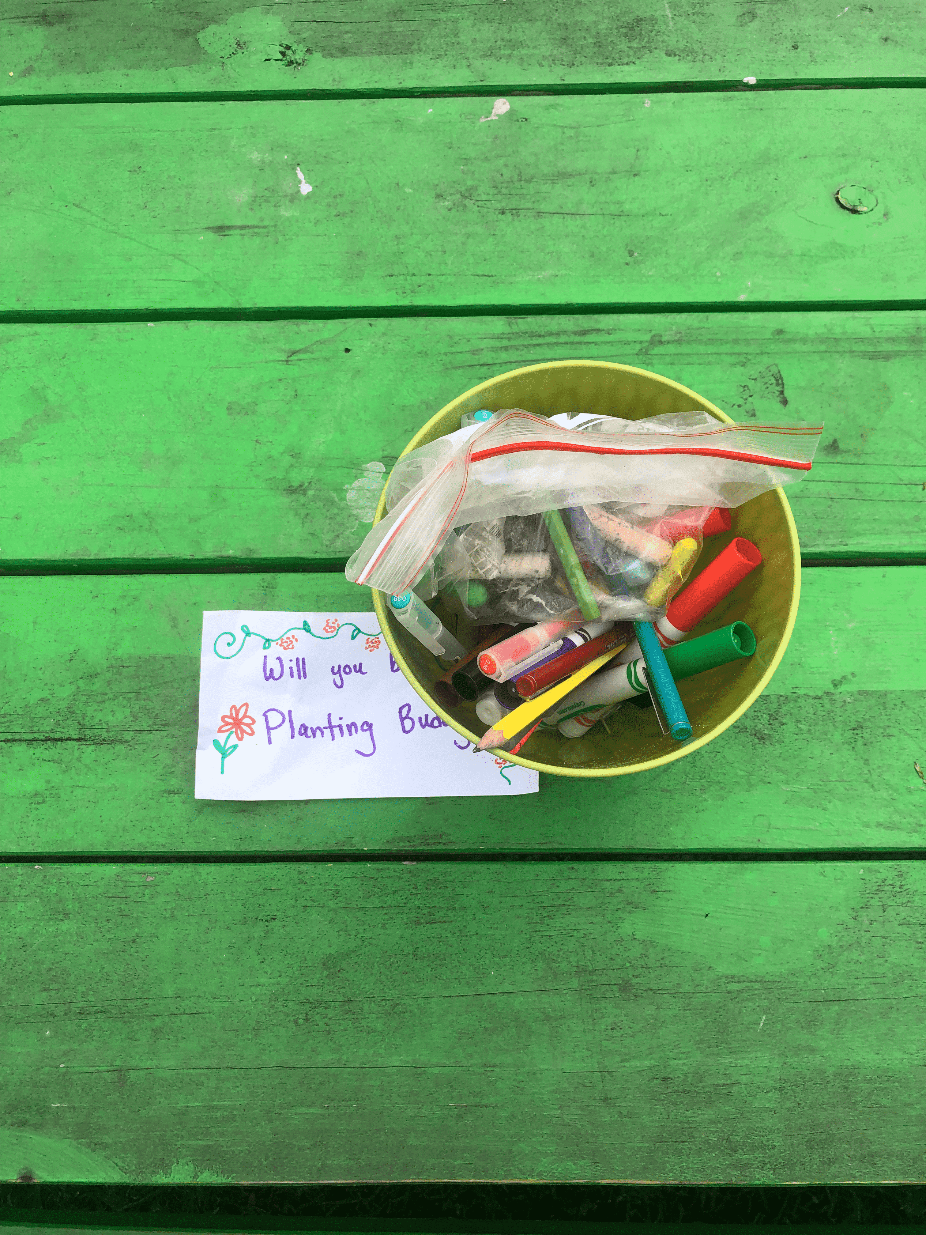 A close-up picture of a small metal bucket full of colorful writing utensils on a bright green table