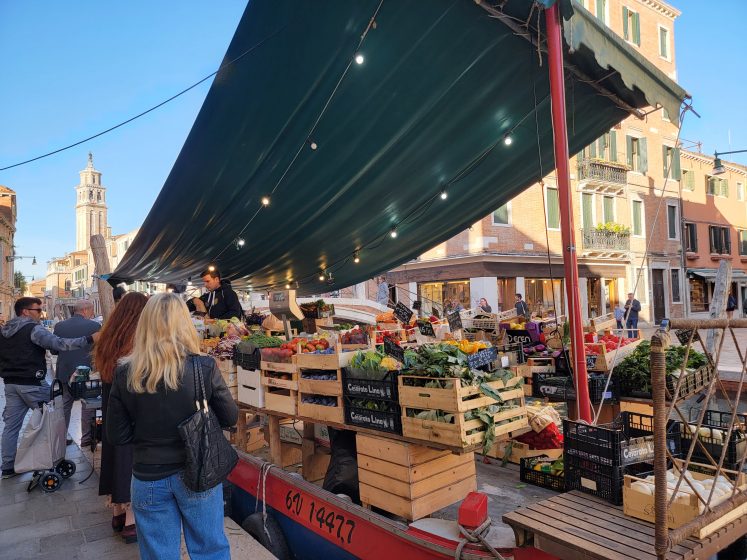 A picture of a produce stall with people standing and walking