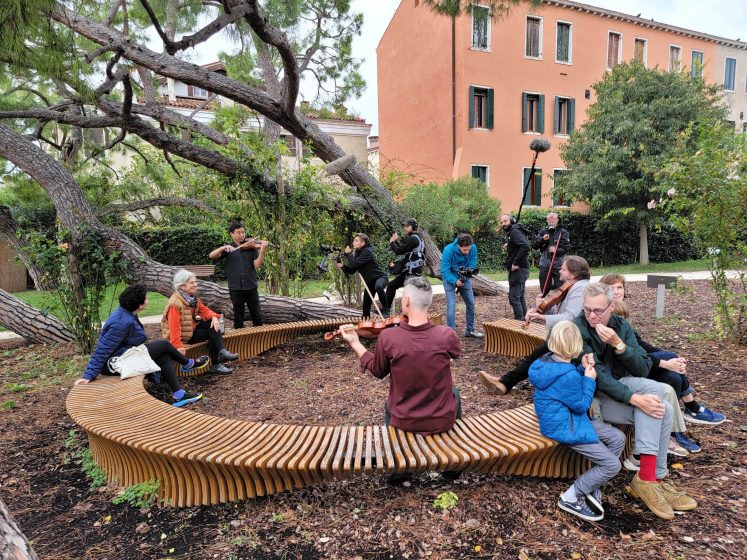 A picture of several people sitting on a large round bench in a city park