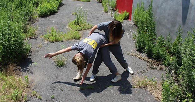 A person stretching another person in a concrete outdoor area