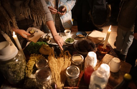 A table full of dried herbs, glass jars, candles, and food