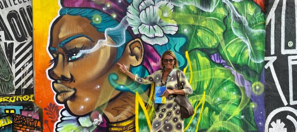 A woman standing in front of a brightly colored mural of a woman's head