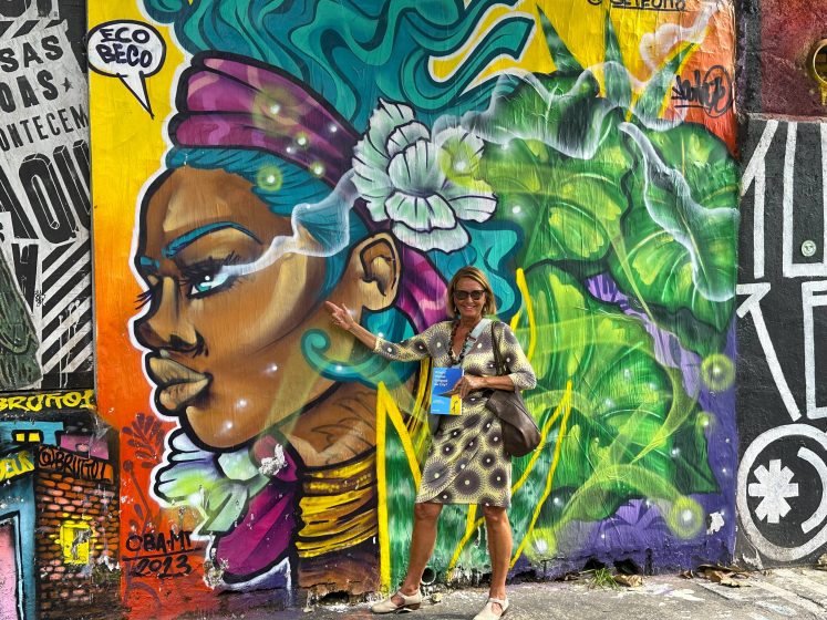 A woman standing in front of a brightly colored mural of a woman's head