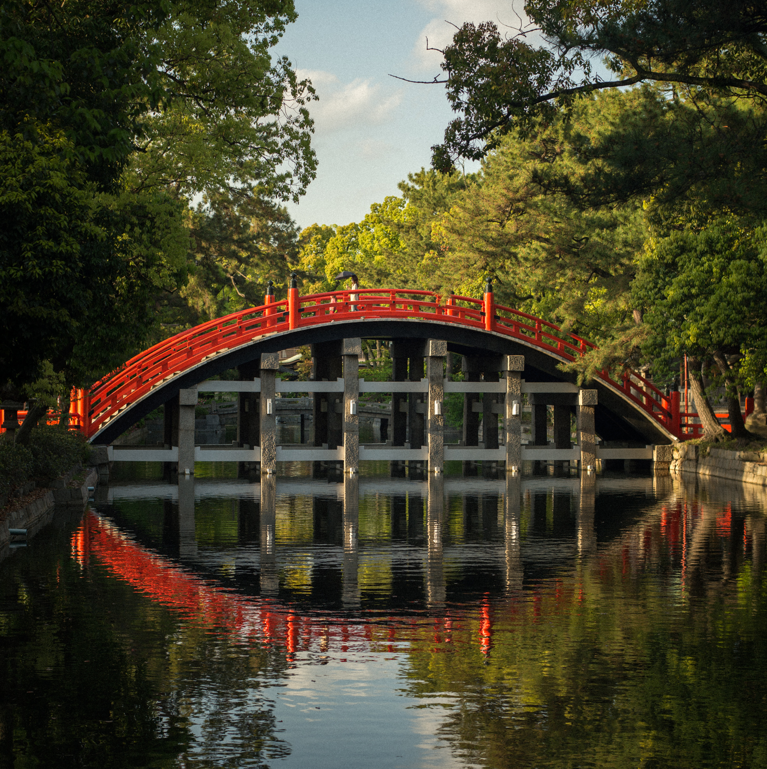 A red bridge over a river with trees on either side