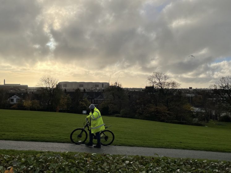 A person in a hi-vi jacket walking next to a bicycle on a path through a field