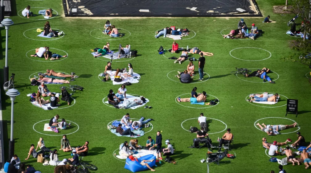 A picture of many people sitting in the grass inside painted circles, all six feet apart
