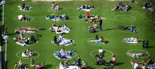 A picture of many people sitting in the grass inside painted circles, all six feet apart