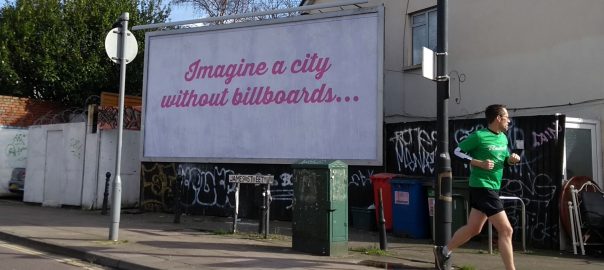 A billboard in pink script reading "Imagine a city without billboards" with a person in activewear running by it