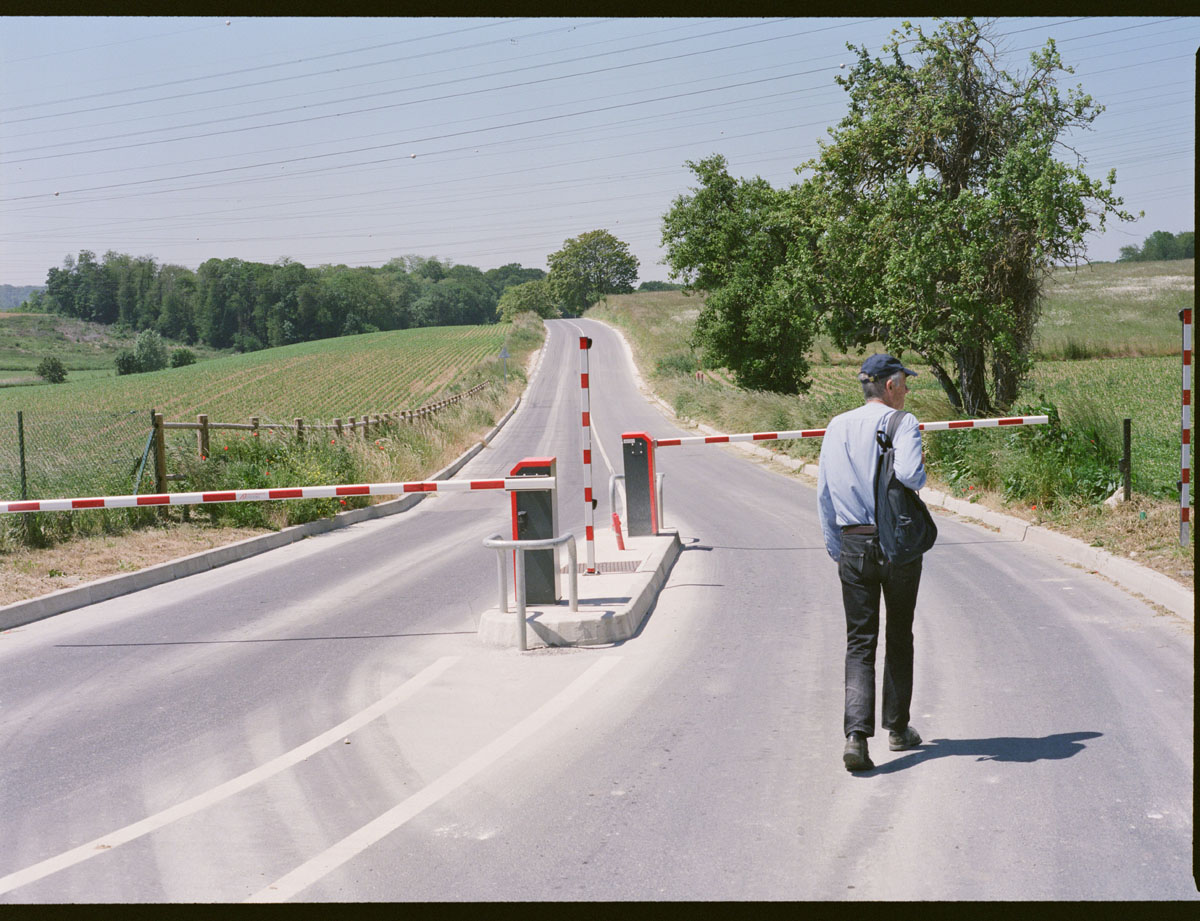A picture of a person walking down a paved road with traffic gates in the distance