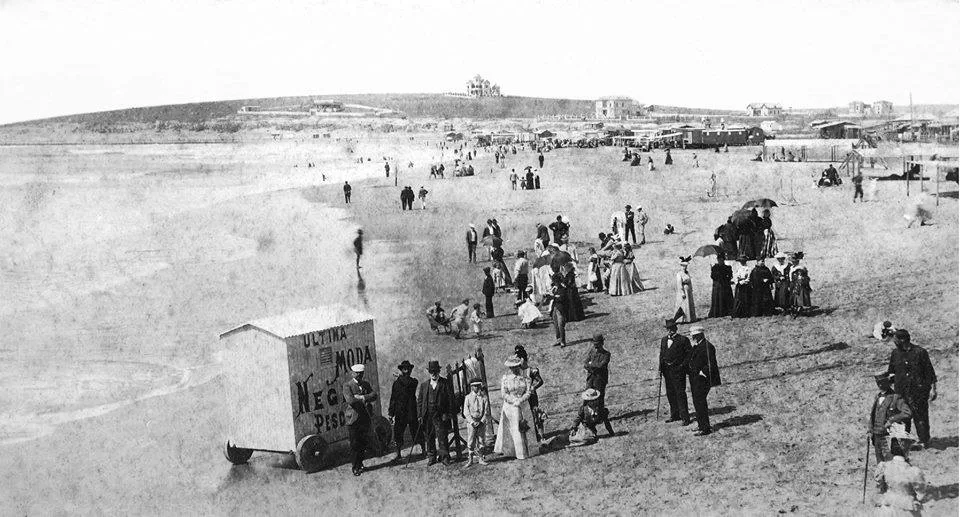 A black and white picture of a large group of people on a beach enjoying the sand and water