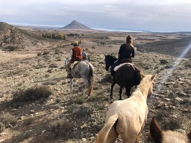 A group of people riding horses on a dirt road through a rocky plains