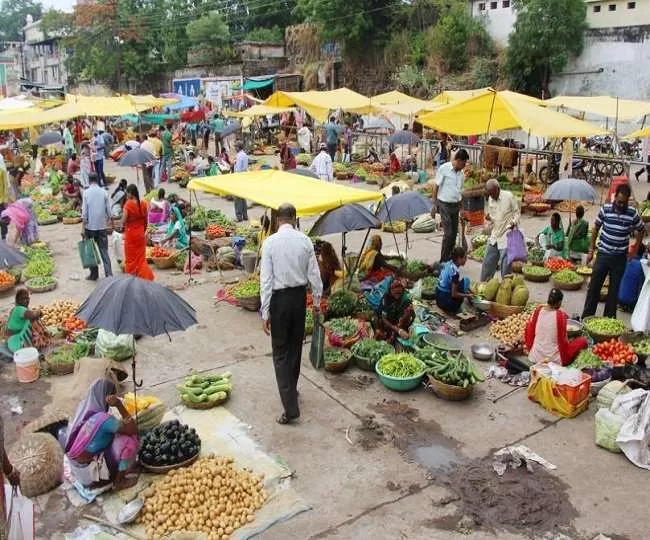 A person walking amongst an open air food market with multiple vegetable stalls and colorful umbrellas