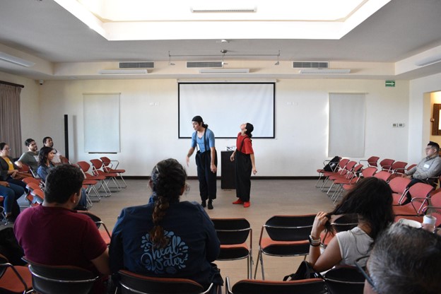 Two people performing in a small room in front of a crowd