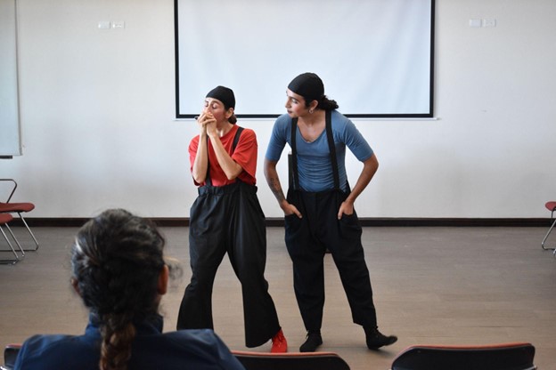 Two people performing in a small room in front of a crowd