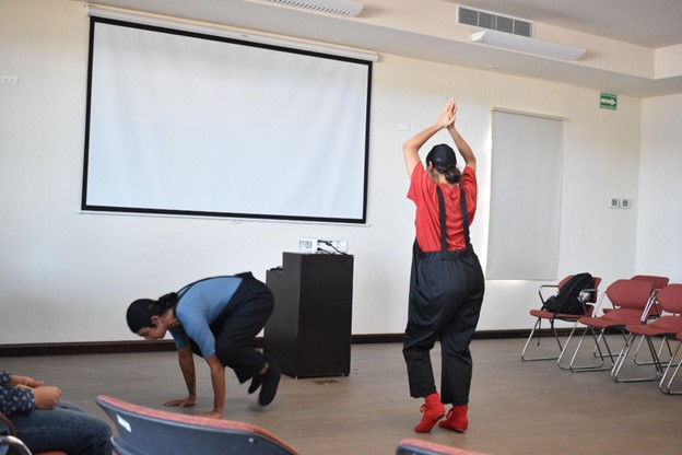 Two people performing in a small room in front of a crowd