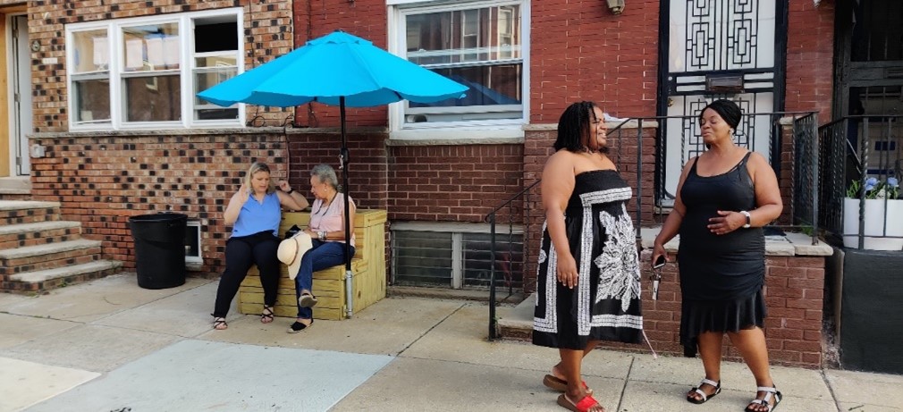 People sitting and standing on the sidewalk outside of a brick building