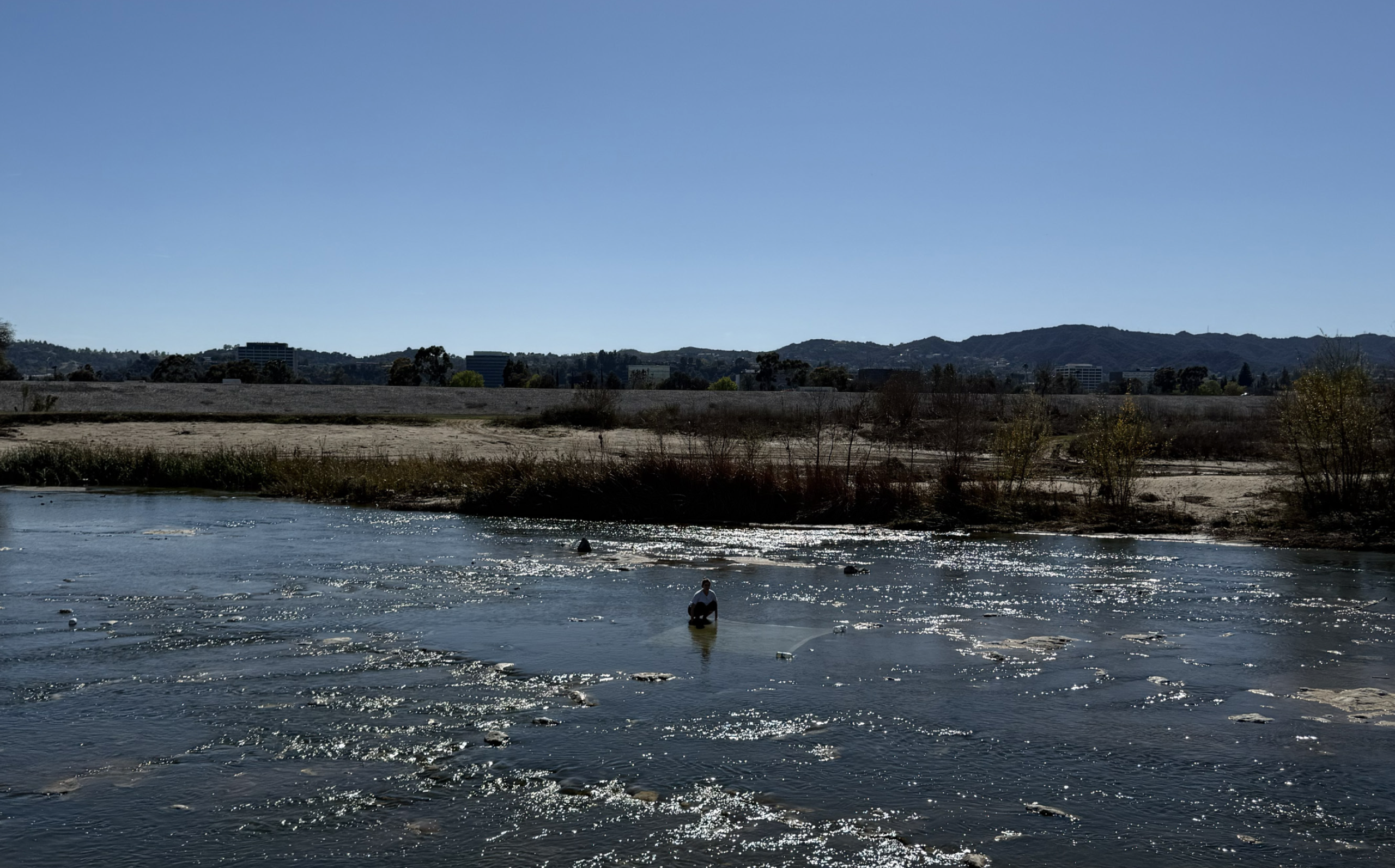 A large blue river with a person crouching in the river far in the distance
