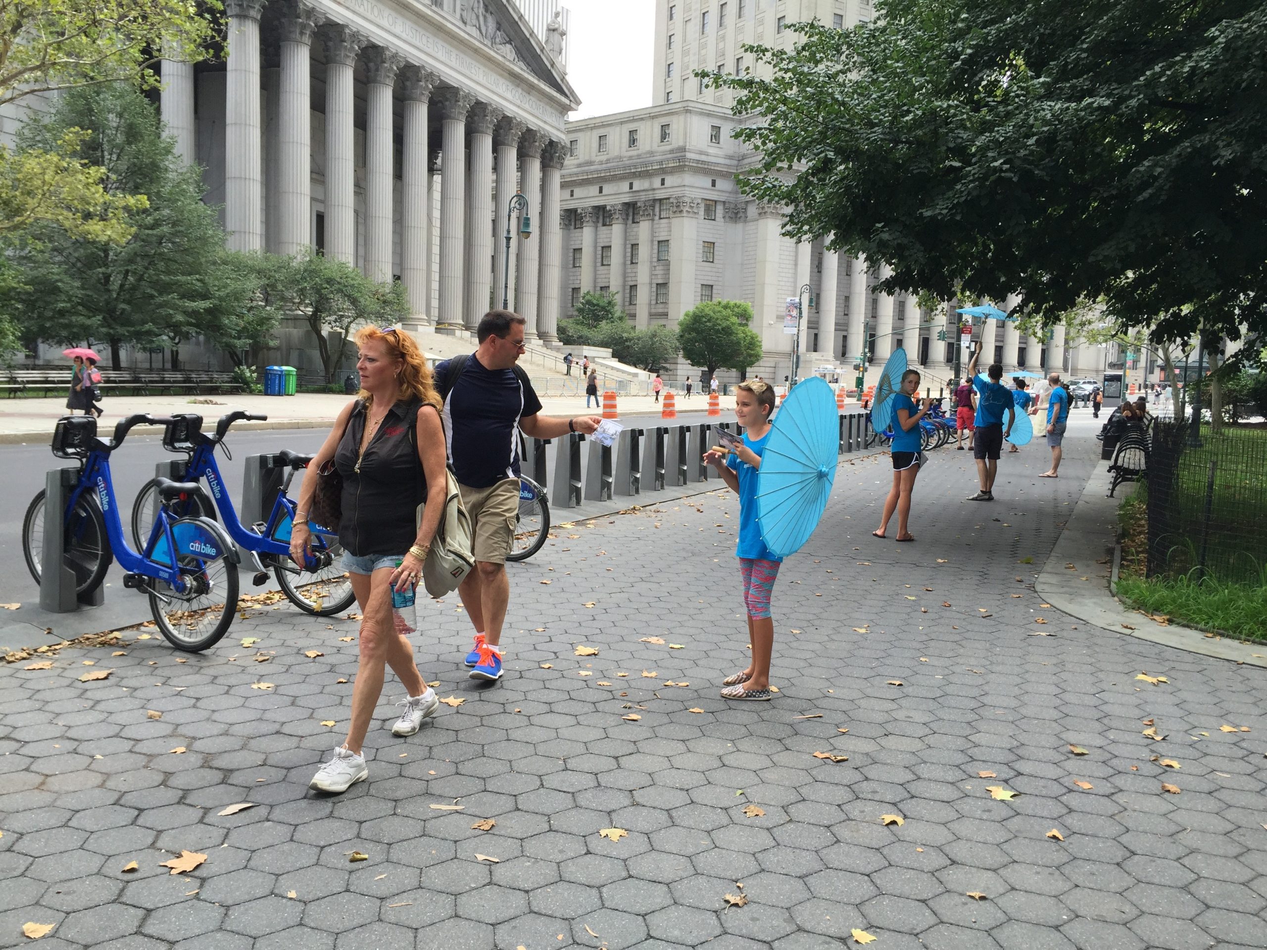 A small group of people walking on a sidewalk with a bike rack