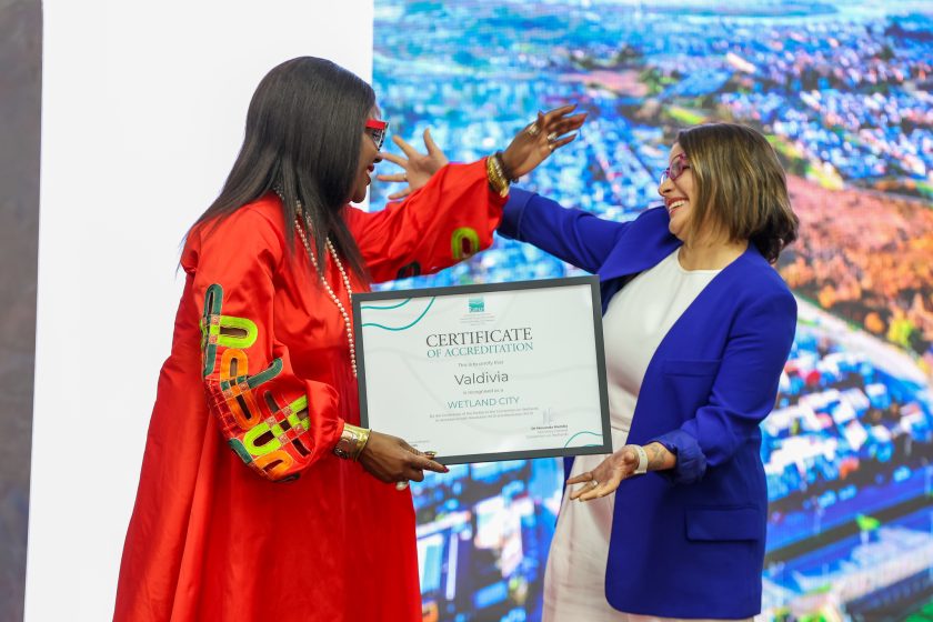 Two people in the act of embracing and exchanging a framed certificate 
